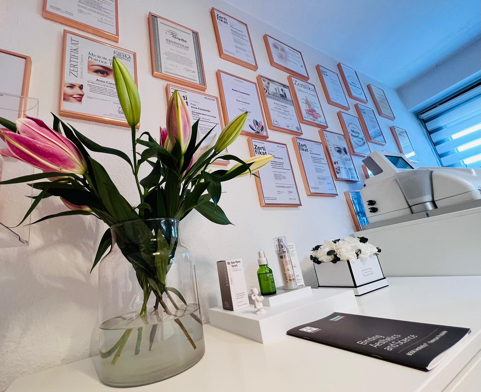 Zertifikatwand im Kosmetikstudio von Anne Constantin mit Blumenstrauß und Hautpflegeprodukten